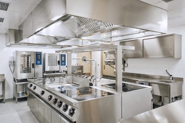 Cucina Mareno completa in acciaio inox. Blocco cottura centrale con forni e linee di preparazione.